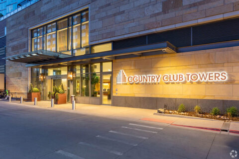 Street entrance to Country Club Tower with glass walls, bright lights, and lighted monument signage.