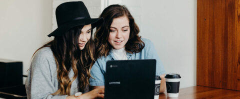 Two friends working together on laptop computer at coffee shop.