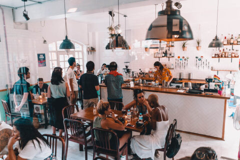 Busy bar with white tile walls and large lamps bustling with customers.