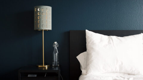 Plush bed with black headboard in front of blue accent wall and bedside table with lamp and water bottle.